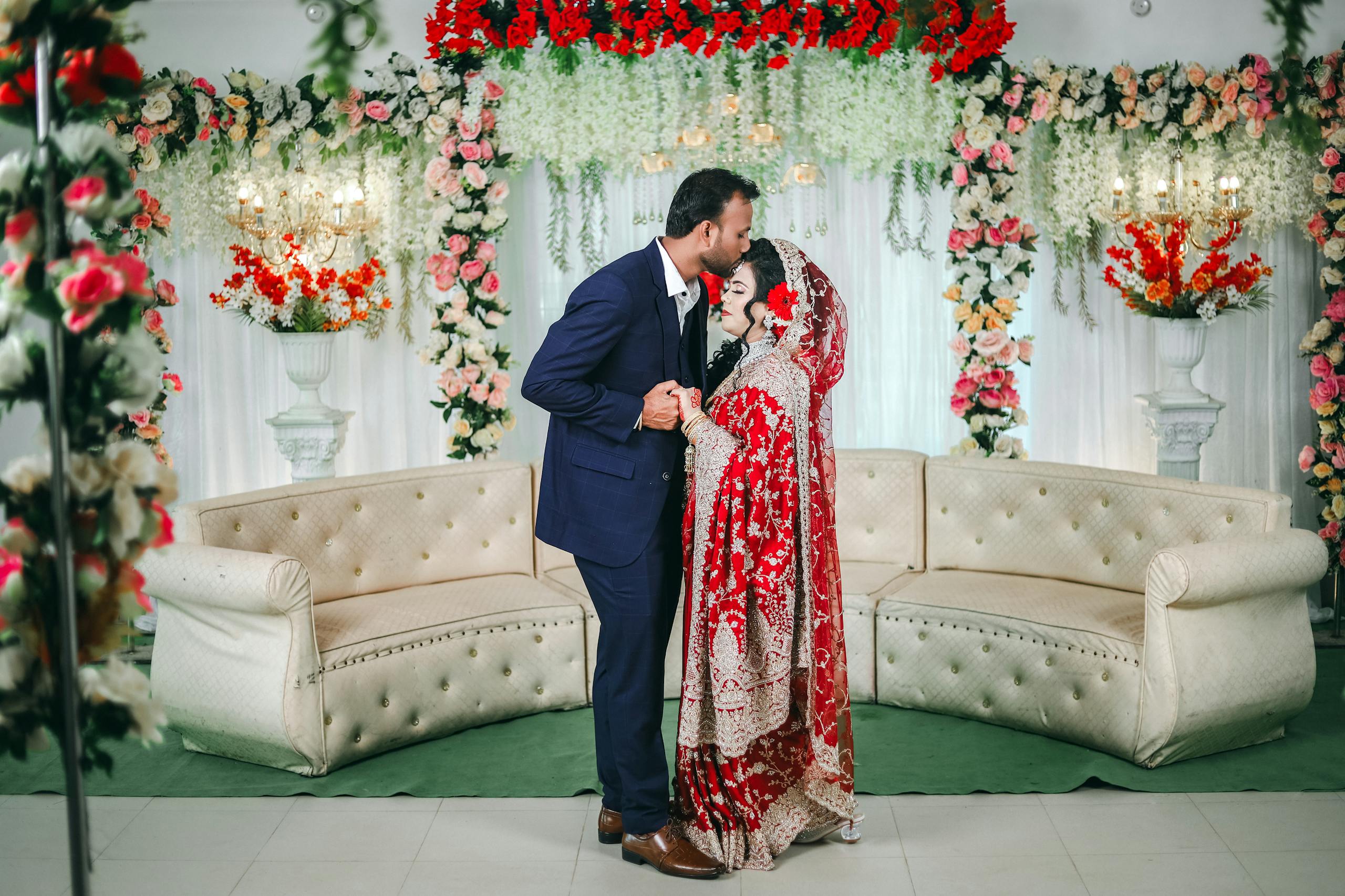 A beautiful South Asian couple during their wedding ceremony indoors, surrounded by elegant floral decorations.