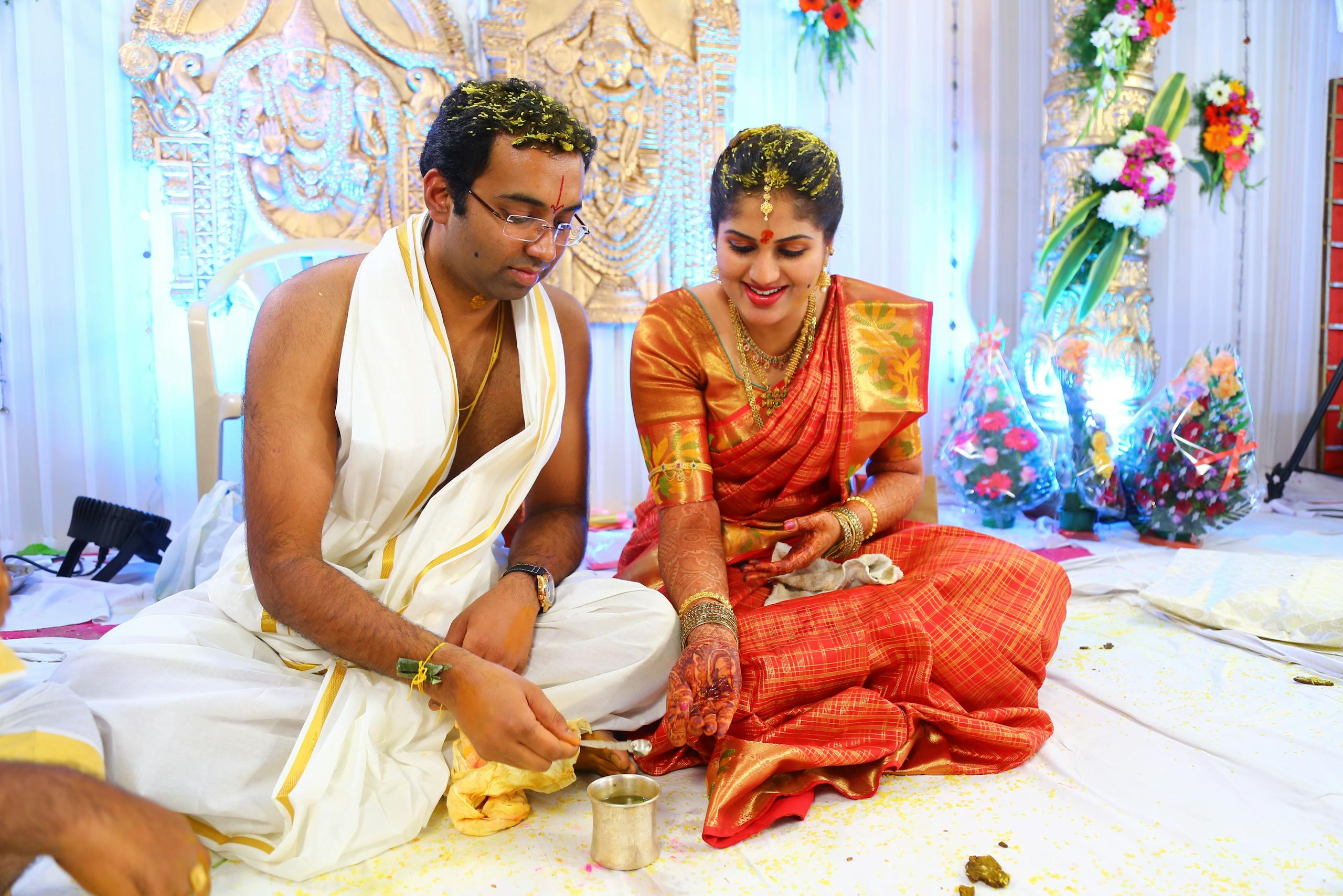 A couple performing traditional rituals in vibrant Indian wedding attire, smiling together.