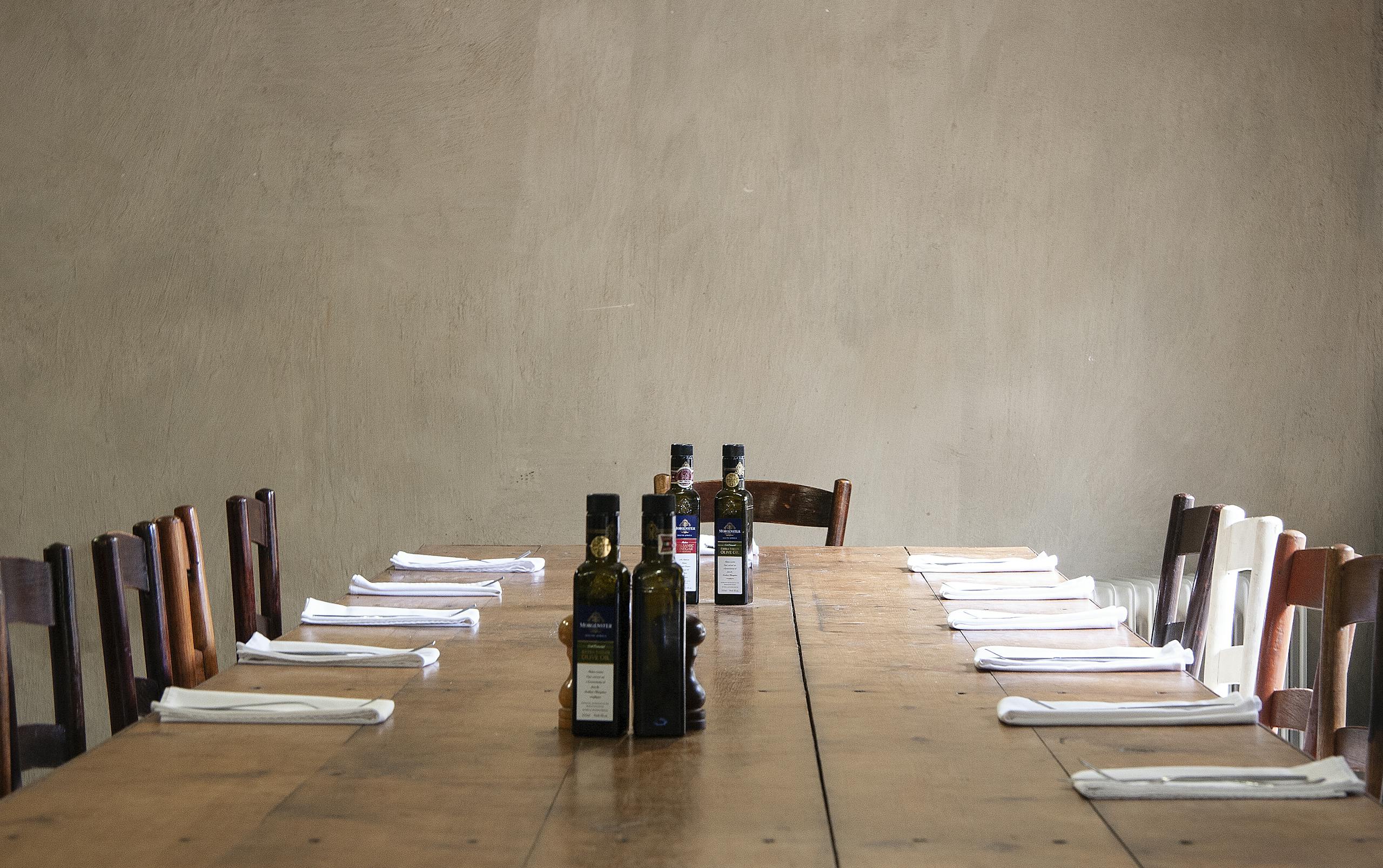 A long dining table set with napkins, olive oil bottles, and wooden chairs, ready for a feast.