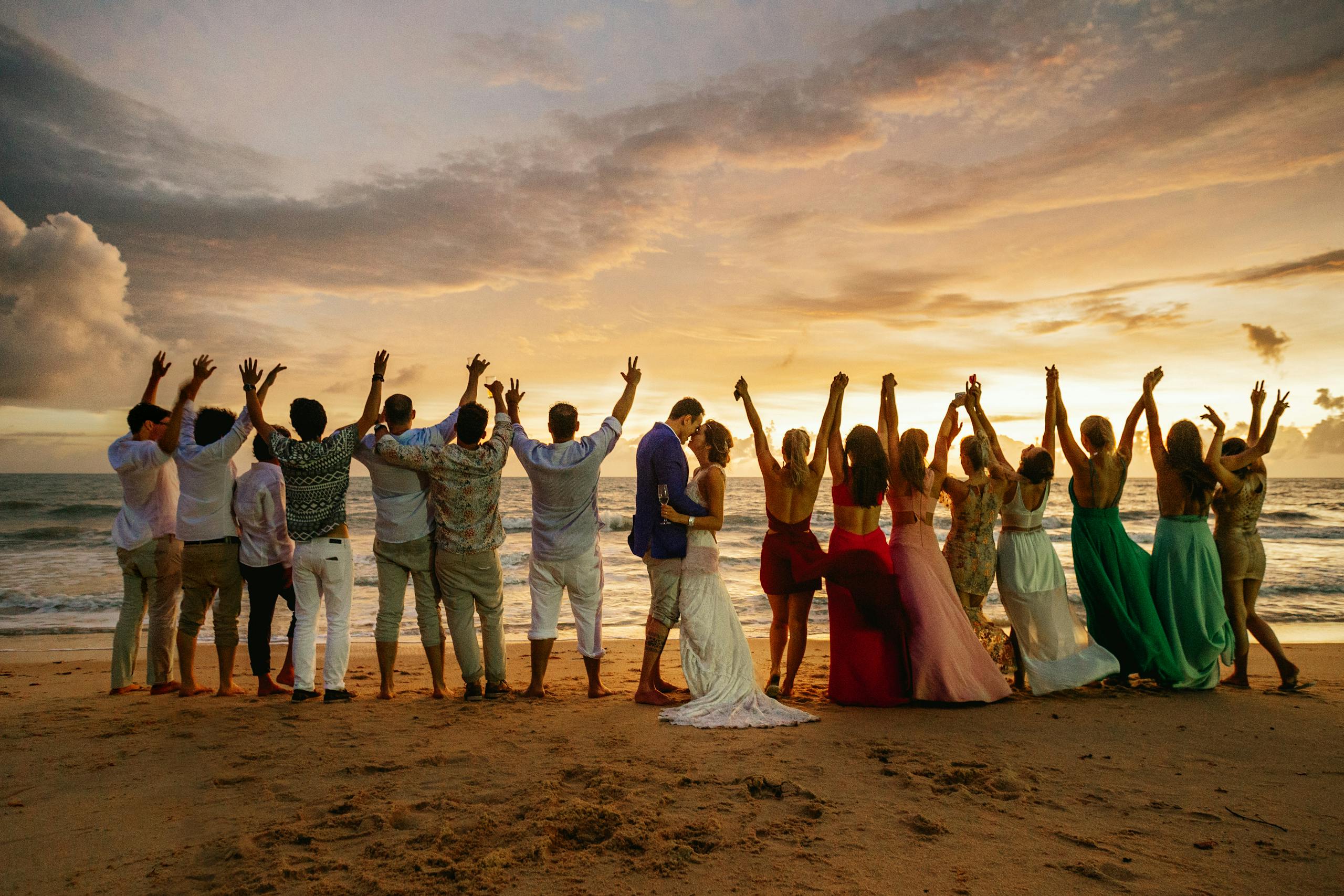 Couple with wedding party on beach at sunset, capturing joy and romance.
