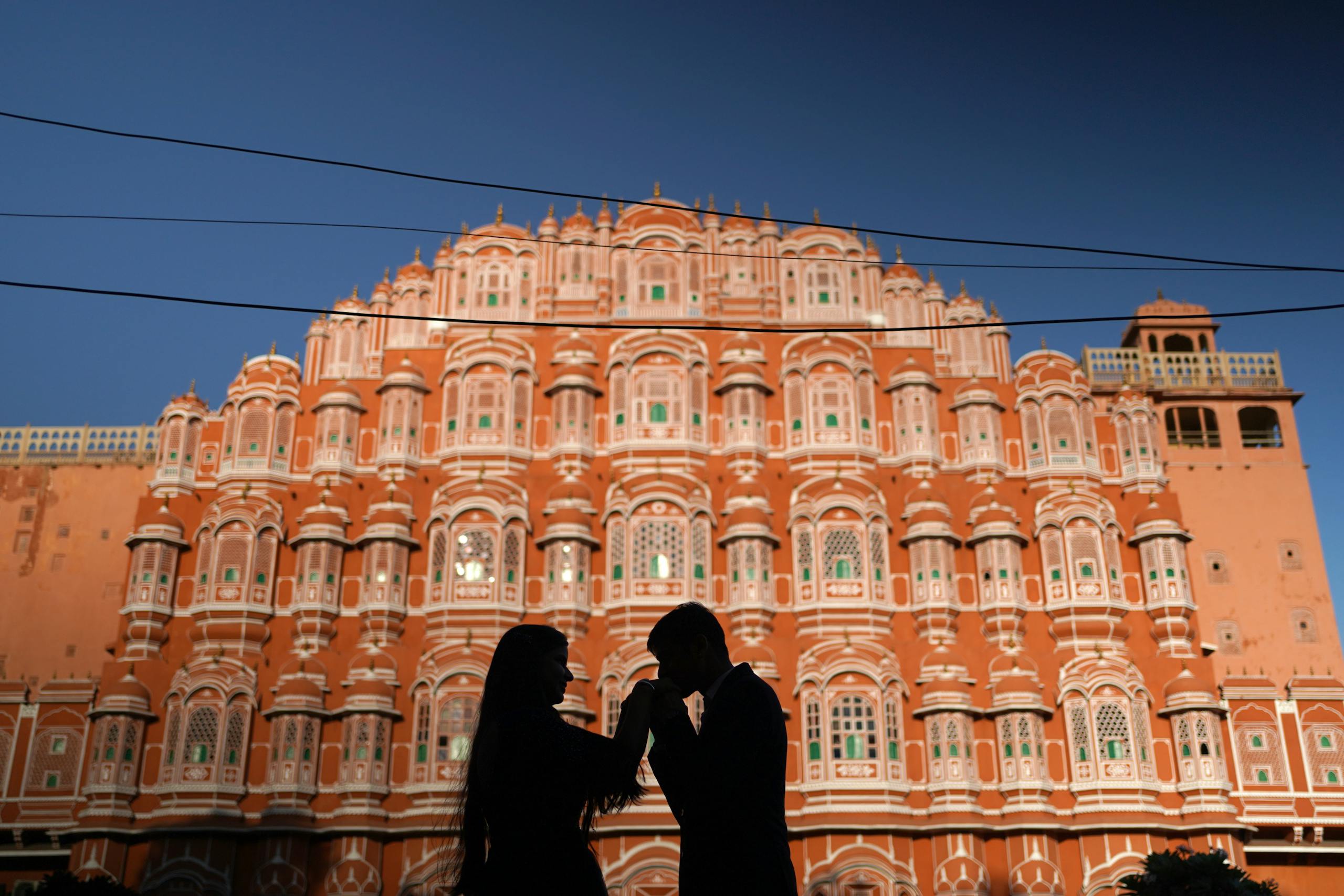 Silhouette of a romantic couple kissing in front of the iconic Hawa Mahal in Jaipur, India.