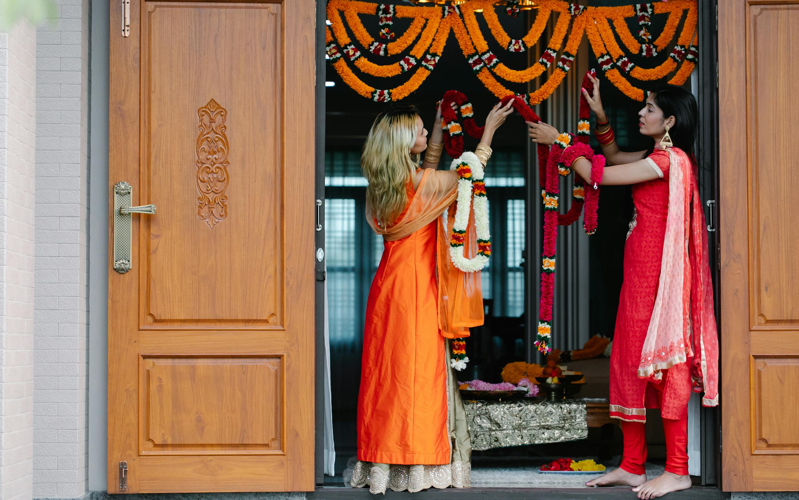 Women decorating a doorway with flowers for a traditional Indian festival.